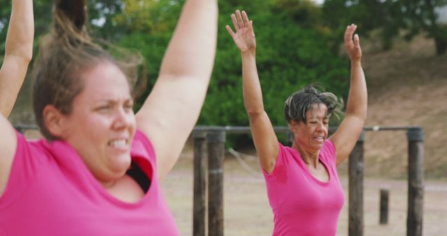 Two happy caucasian female friends in pink t shirts doing jumping jacks, training at bootcamp. Female fitness, challenge and healthy lifestyle.