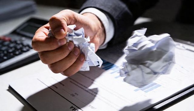 Business frustration: hand crumpling financial report over calculator and bar chart