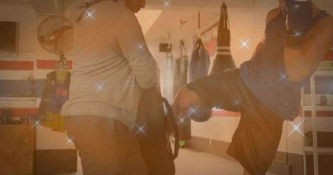 Coach holding kick shield while athlete delivers knee strike in boxing gym