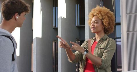 Young students chatting and pointing on modern university campus with urban architecture