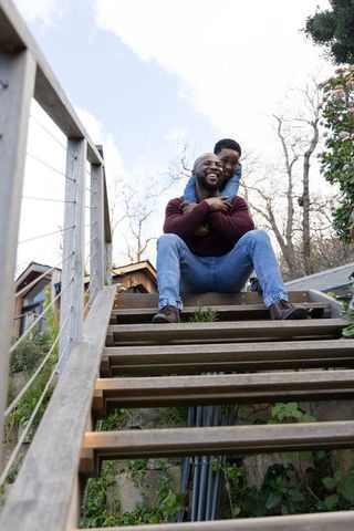 African american father and son sharing laugh on outdoor stairs, cozy family bonding moment