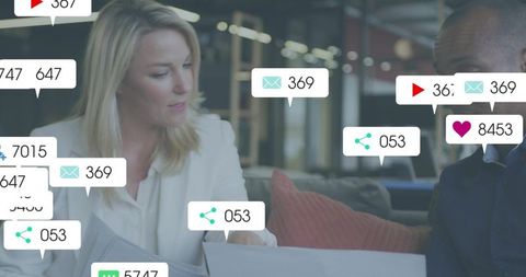 Reviewing documents and laptop in open-plan office with social media notifications overlay