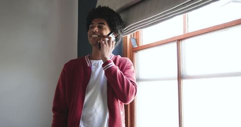 African American Man Talking on Phone by Sunlit Window in Red Jacket, Casual Lifestyle