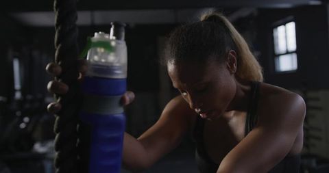 Athletic woman resting with battle rope in dark gym