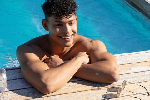 Smiling african american man leaning on pool edge enjoying sunny backyard relaxation