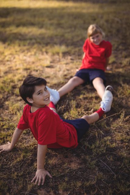 Happy kids relaxing on grass during obstacle course in boot camp