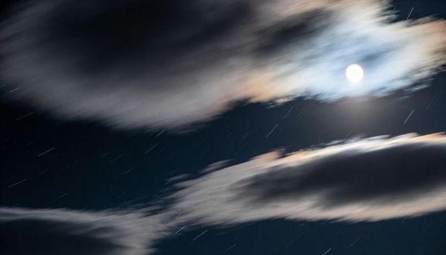 Moonlit clouds racing across night sky with haloed moon and dramatic star trails