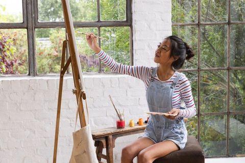 Young asian woman painting on easel in art studio with natural light