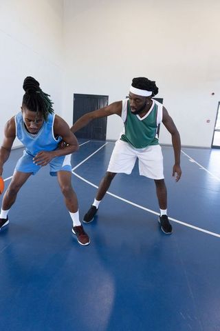 Two male athletes playing intense basketball on indoor court in stylish jerseys