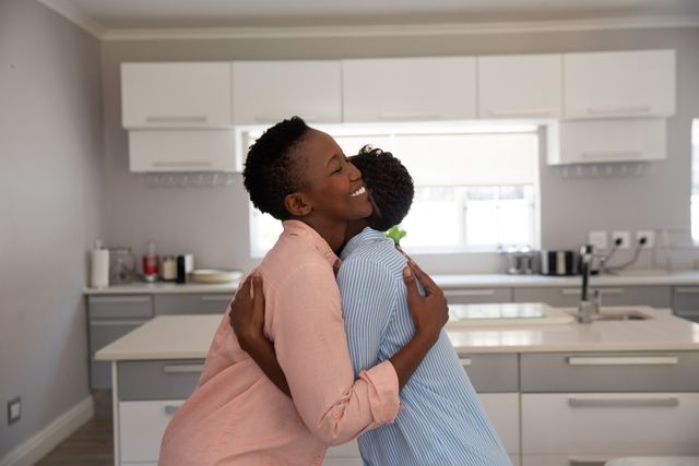 African American mother and daughter embracing and smiling in the kitchen of their home. Family and domestic life.