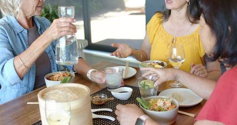 Multigenerational women enjoying casual lunch, pouring water, sharing healthy bowls