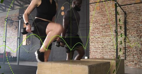 Training partners stepping onto plyo boxes holding dumbbells in industrial gym