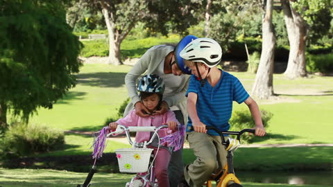 Mother Ensuring Safety While Biking with Children in Park