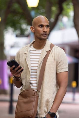 African american man checking smartphone on tree-lined street with leather crossbody bag