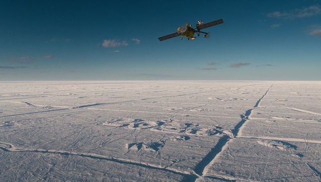 Research aircraft skimming low over Arctic sea ice with landing gear, ice leads and ridges