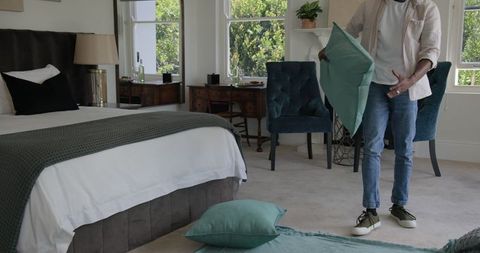 Man Arranging Pillows in Cozy Bedroom for Comfort and Style