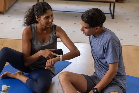 African american friends checking fitness tracker and phone after home workout session