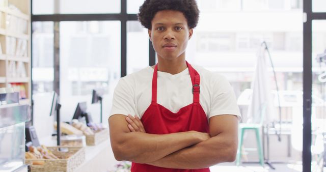 Young grocery store employee standing with arms crossed in front of shelves. Perfect for advertisements, promotional materials for grocery stores, retail job postings, or business service presentations.