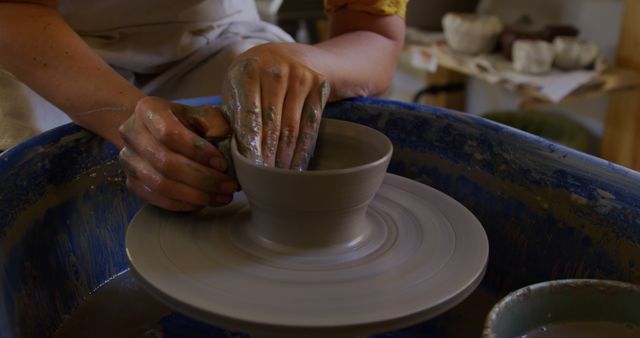 Hands forming clay on a spinning potter's wheel. Ideal for illustrating creative processes, crafts, artistry, workshops, artisan skills, ceramic making, DIY hobby projects, and art studios.