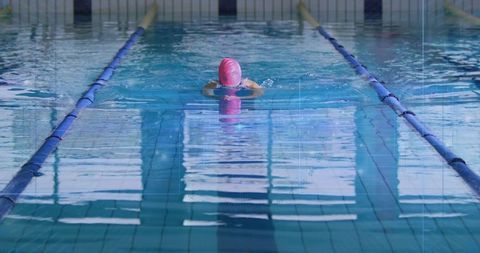 Woman swimming breaststroke in indoor pool with pink swim cap