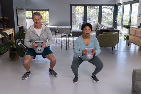 Senior exercise partners using kettlebells in modern living room