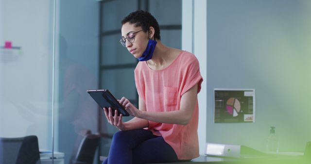 Young woman with face mask using tablet in modern office - Download Free Stock Images Pikwizard.com