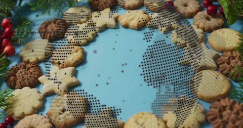 Forming Festive Cookie Wreath on Pale Blue Tabletop with Fir Sprigs and Red Berries