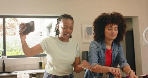 Diverse female friends filming cooking while chopping vegetables in bright kitchen