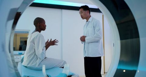 Korean clinician discussing ct scan with female patient sitting on scanner gantry