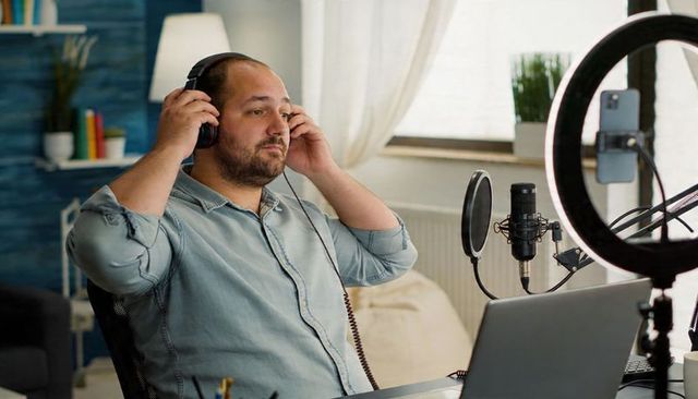 Bearded man adjusting headphones in home podcast studio with condenser mic and ring light