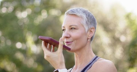 Mature woman speaking into smartphone outdoors wearing smartwatch and athletic top