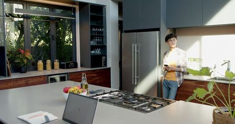 Man Holding Smartphone Relaxing in Modern Kitchen with Sunlight