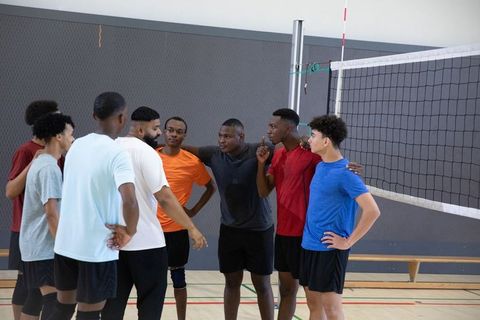 Diverse male teenage volleyball team huddling near net planning strategy in indoor practice