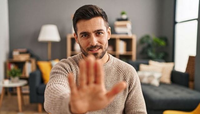 Man reaching toward camera with welcoming gesture in cozy living room warm tones portrait
