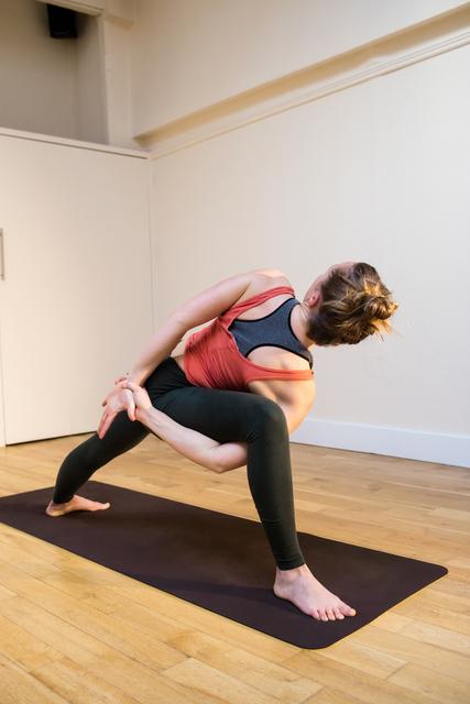 Woman performing bound side angle pose on exercise mat in fitness studio