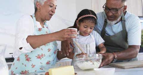 Grandparents Teaching Granddaughter Baking in Bright Home Kitchen Stirring Smiling Happy