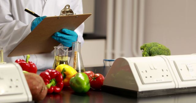 A scientist in a lab coat and gloves takes notes on a clipboard, surrounded by colorful vegetables and lab equipment, with copy space. The setting suggests a research environment focused on food science or agricultural studies.