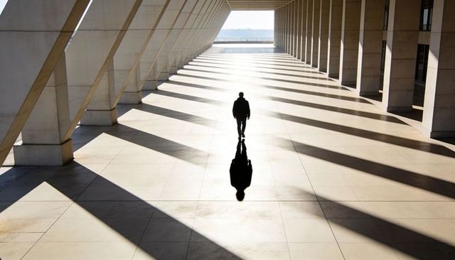Solitary silhouette walking through sunlit colonnade with long dramatic shadows