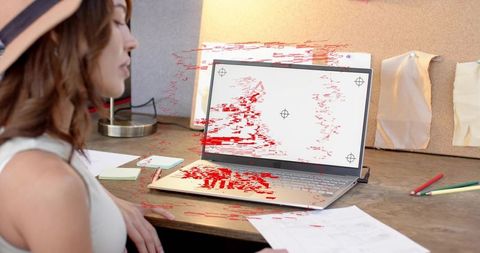 Woman wearing hat viewing glitching laptop screen at creative desk with corkboard and notes