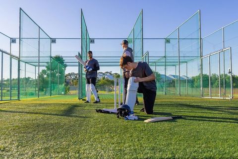 Male cricketers practicing in net lanes on turf adjusting pads and preparing bats for training