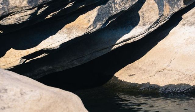 Sunlit granite overhang featuring dark tidal pool and layered rock slabs