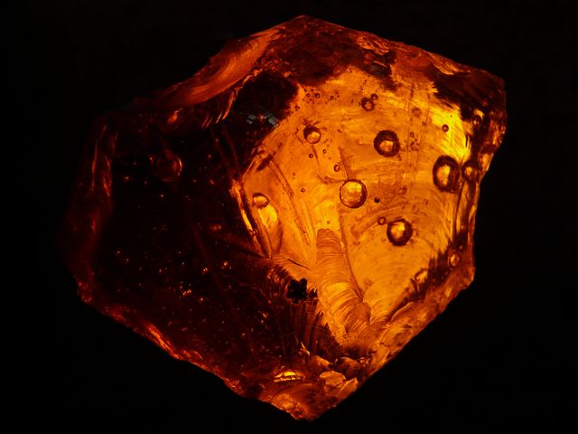 Close-up of an iridescent amber gem, showing intricate glowing patterns and textures. This image highlights a vibrant and detailed view of the amber, making it suitable for use in blogs or articles related to geology, gemology, natural history, or decoration. The unique, glowing patterns add an artistic aesthetic, which is perfect for design, jewelry advertisements, and educational purposes.