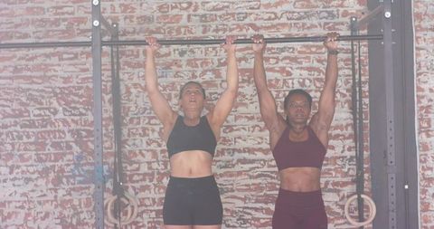 Two Women Hanging from Pull-Up Bar Showing Upper-Body Strength and Partner Training