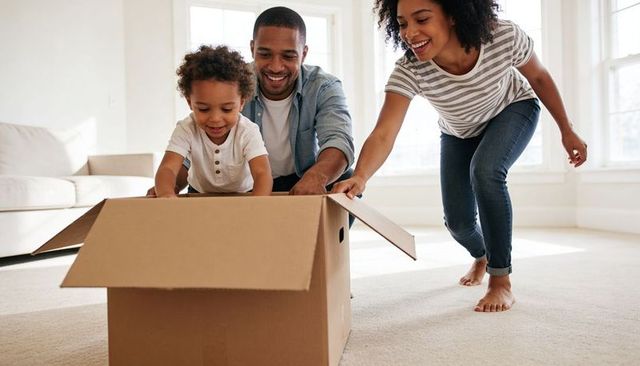 Playing with moving box: joyful young family unpacking with toddler and laughing in sunlit new home