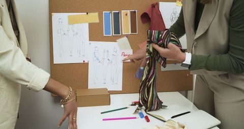 Fashion designers collaborating over striped fabric swatch and corkboard sketches