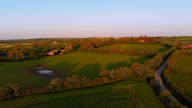 Aerial view of picturesque farmland surrounded by autumn trees and greenery on a bright, sunny day. Perfect for articles and blogs focused on rural life, agriculture, nature, and travel destinations. Great visual for brochures promoting countryside retreats and outdoor activities.