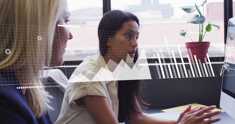 Collaborating on analytics: woman pointing at monitor with overlaid charts in modern office