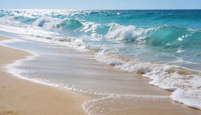 Rolling turquoise waves meeting sunlit sandy shoreline with sparkling white foam