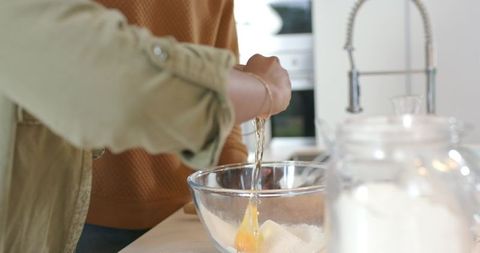 African American couple cracking egg and sifting flour while baking on sunlit counter