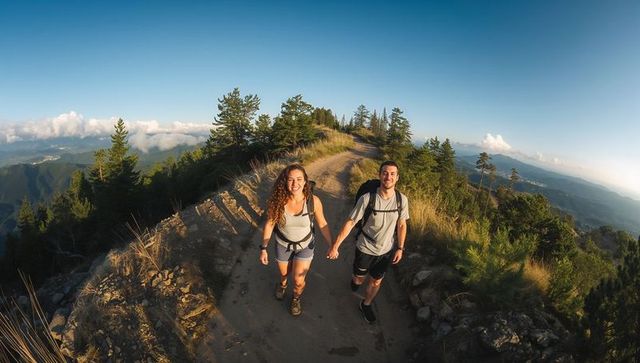 Couple hiking mountain ridge trail at golden hour holding hands with backpacks and pine forest